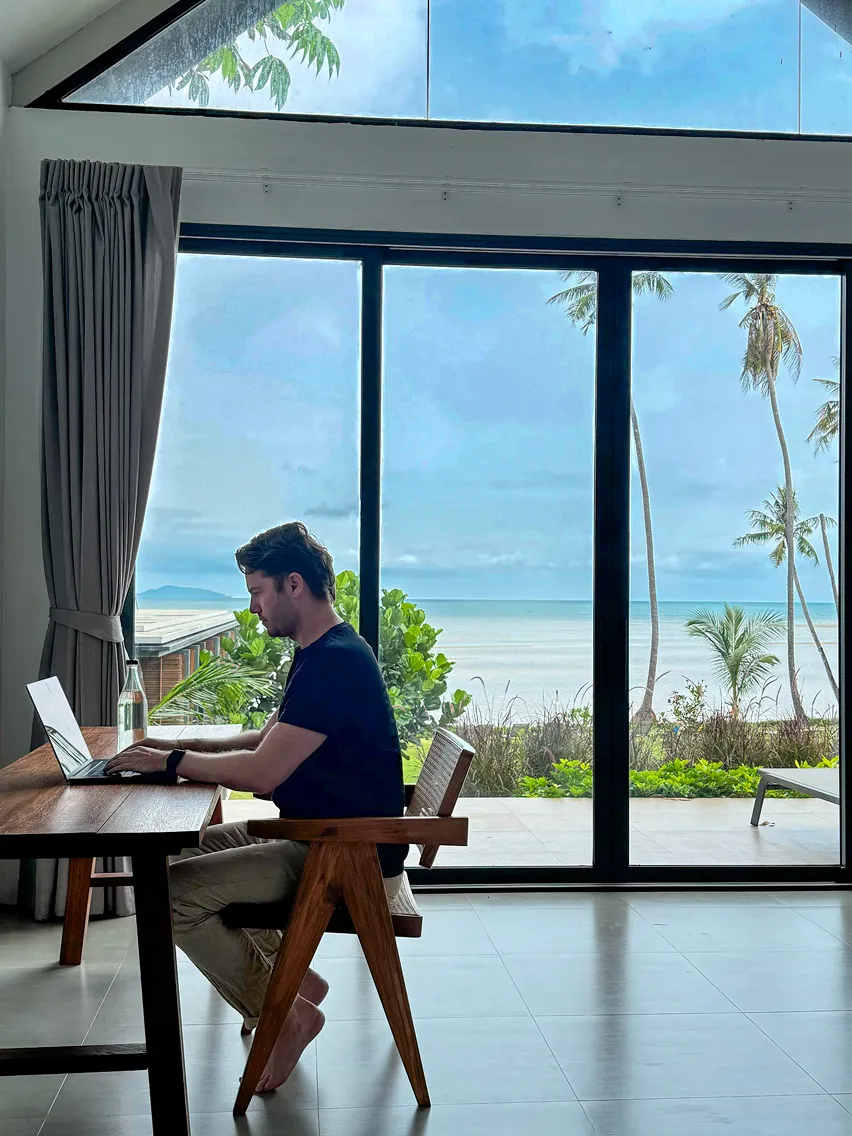 Chris arbeitet konzentriert am Laptop mit Blick auf das Meer. Workation-Moment zwischen Fokus, Ruhe und Inspiration.