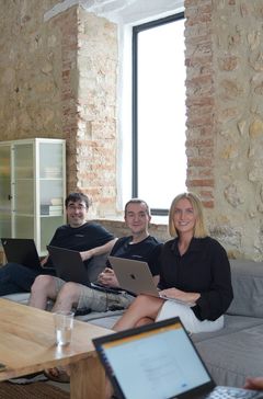 Drei Teammitglieder sitzen mit Laptops auf einem Sofa im Büro.